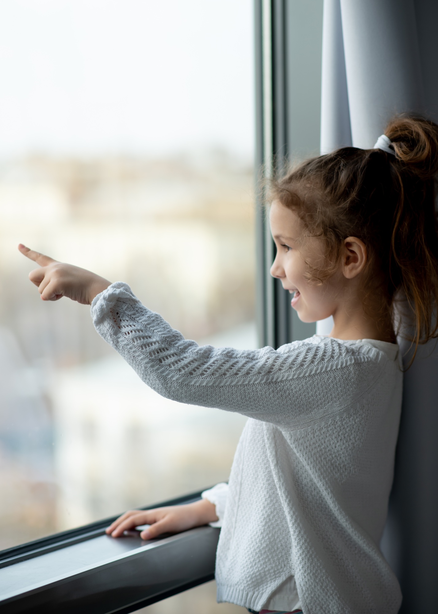 A cute little girl looks out the window. House. Comfort. Atmosphere.